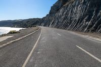 a motorcycle on the road near water with no people nearby and a cliff side in the background