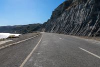 a motorcycle on the road near water with no people nearby and a cliff side in the background