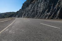 a motorcycle on the road near water with no people nearby and a cliff side in the background