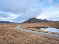 an empty road leads to the top of a mountain, with small river and mountains in the distance