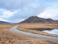 an empty road leads to the top of a mountain, with small river and mountains in the distance