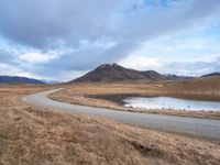 an empty road leads to the top of a mountain, with small river and mountains in the distance