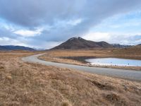 an empty road leads to the top of a mountain, with small river and mountains in the distance