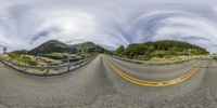 a fish - eye lens view of a road with mountains in the back ground and trees on the other side