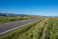 a view of a country road running along a cliff with green grass and plants on either side