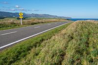 a view of a country road running along a cliff with green grass and plants on either side