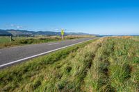 a view of a country road running along a cliff with green grass and plants on either side