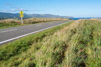 a view of a country road running along a cliff with green grass and plants on either side