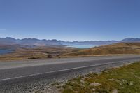 a car on the road next to some mountains and a large lake in the distance