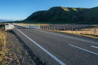 a fenced in street near the edge of a mountainous field of grass and hills