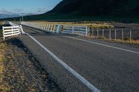 a fenced in street near the edge of a mountainous field of grass and hills