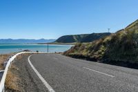 an empty road by the ocean near a hilly hill with many mountains in the background