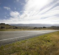 a long empty roadway is surrounded by tall grasses on the ground and the sky in the distance
