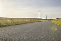 a road in the middle of a rural area, with telephone poles in the distance