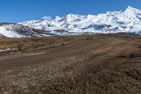 a person is walking across the gravel road and mountains in the distance, and the snow is clearly visible