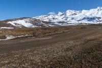 a person is walking across the gravel road and mountains in the distance, and the snow is clearly visible