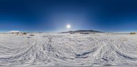 a snow covered ground with rocks and snowy hills in the distance and sun shining above