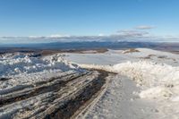 a view down to snow - covered road on a hilltop in the distance, and a man stands on top of it looking over the snow