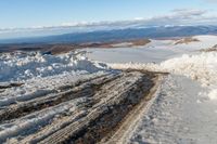 a view down to snow - covered road on a hilltop in the distance, and a man stands on top of it looking over the snow