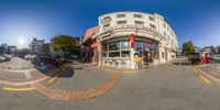 a fish eye view of a corner retail store in a busy town square with the sky visible