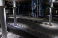 an empty bus station with traffic in it at night time with lights shining brightly on the glass windows