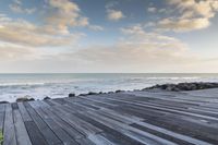 wood walkway beside beach with waves crashing on rocks and blue sky with clouds in background