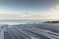 wood walkway beside beach with waves crashing on rocks and blue sky with clouds in background