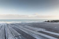 wood walkway beside beach with waves crashing on rocks and blue sky with clouds in background