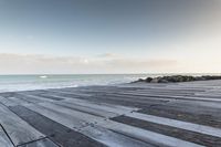 wood walkway beside beach with waves crashing on rocks and blue sky with clouds in background