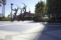 a red metal sculpture sits in front of several trees, and has many colors in it