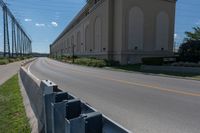 a street and two rows of cement barriers in front of a beige building, and an empty street with cars going by