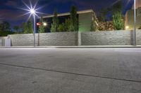 an empty parking lot with street lights and a stone building in the background at night