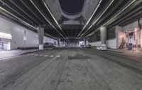 an empty street in the night as cars pass through it below a bridge as if the sun goes down