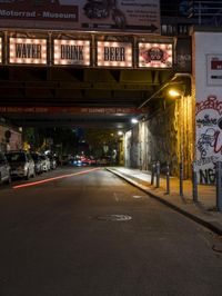 some cars parked on the street next to a bridge and some graffitied walls with neon lights