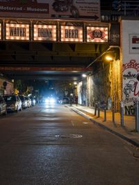 some cars parked on the street next to a bridge and some graffitied walls with neon lights