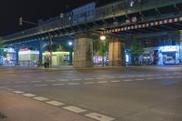 a street at night with people walking and cars on the road below a bridge at night