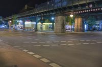 a street at night with people walking and cars on the road below a bridge at night