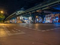 the empty street is filled with people walking and biking under an overpass at night