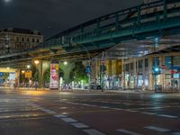 the empty street is filled with people walking and biking under an overpass at night