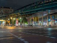 the empty street is filled with people walking and biking under an overpass at night