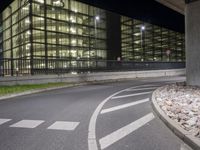 a paved street next to an urban building at night with rocks on the ground and lights in