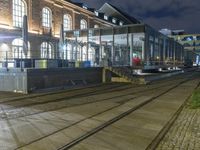 a train passing by an empty building at night on tracks in the street under the lights