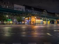 the empty street is filled with people walking and biking under an overpass at night