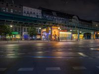 the empty street is filled with people walking and biking under an overpass at night