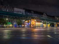 the empty street is filled with people walking and biking under an overpass at night