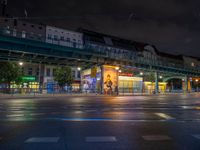 the empty street is filled with people walking and biking under an overpass at night