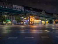 the empty street is filled with people walking and biking under an overpass at night