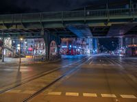 the empty street is filled with people walking and biking under an overpass at night