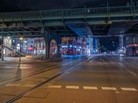 the empty street is filled with people walking and biking under an overpass at night