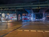 the empty street is filled with people walking and biking under an overpass at night